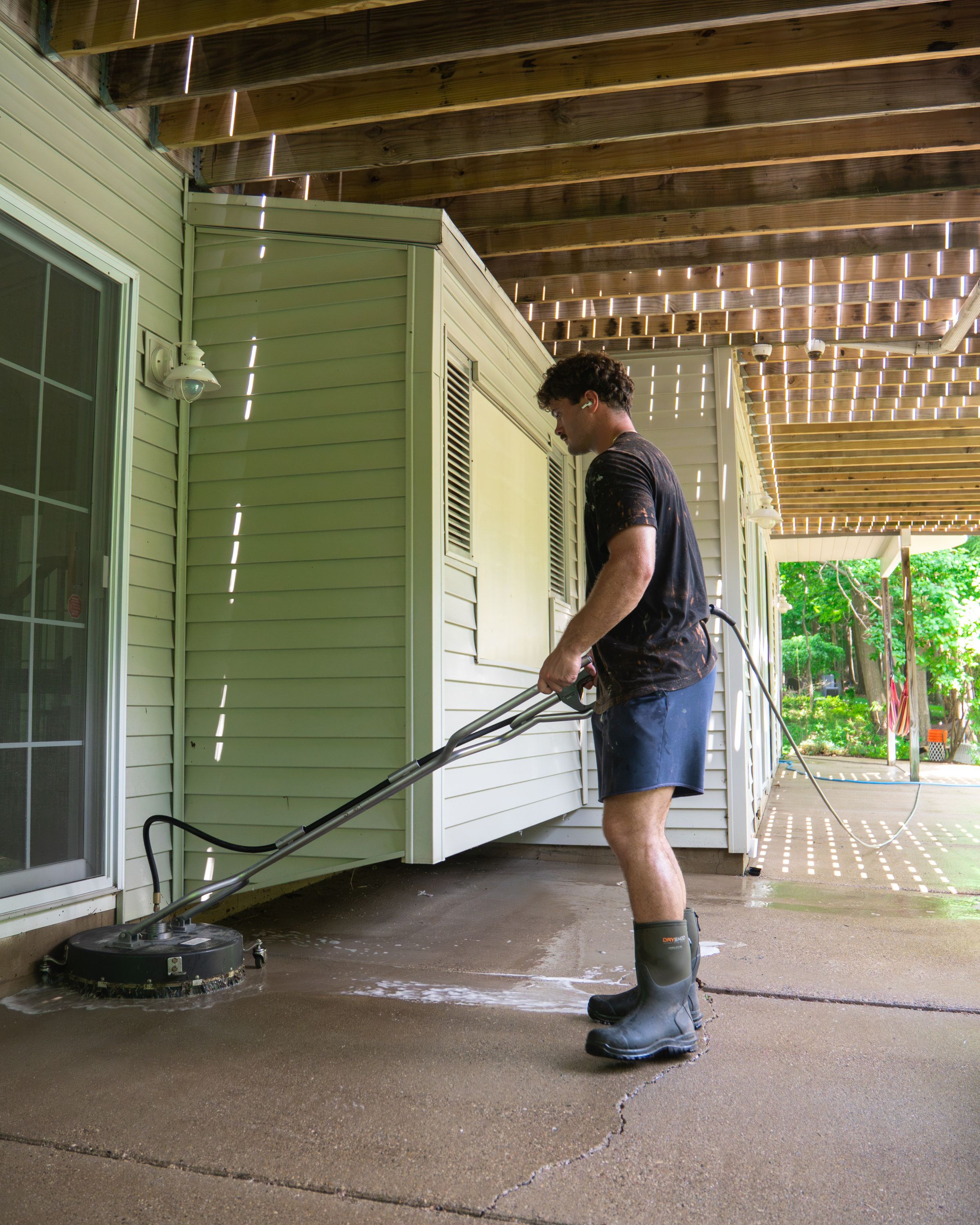 Elevation technician running a rotary surface cleaner across a concrete patio beneath a raised deck