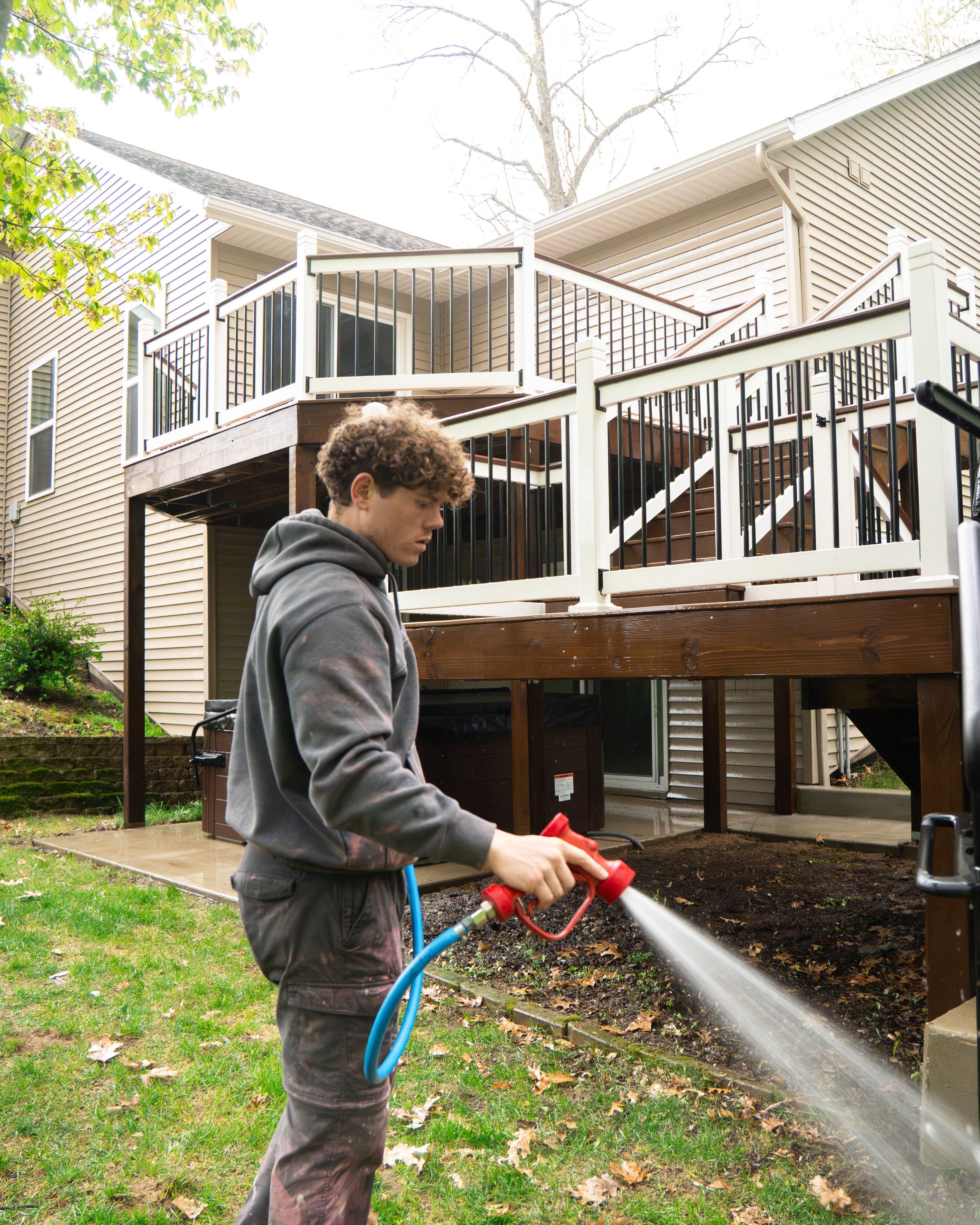 Elevation technician washing beside a two-tier stained wood deck with white vinyl railings