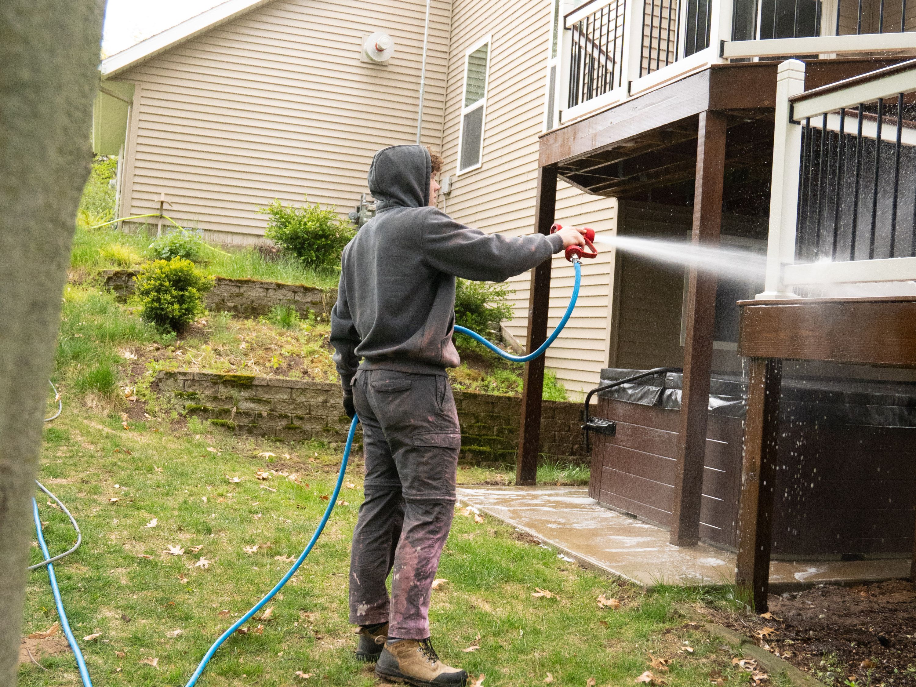 Elevation technician washing the underside and posts of a raised deck with a low-pressure spray