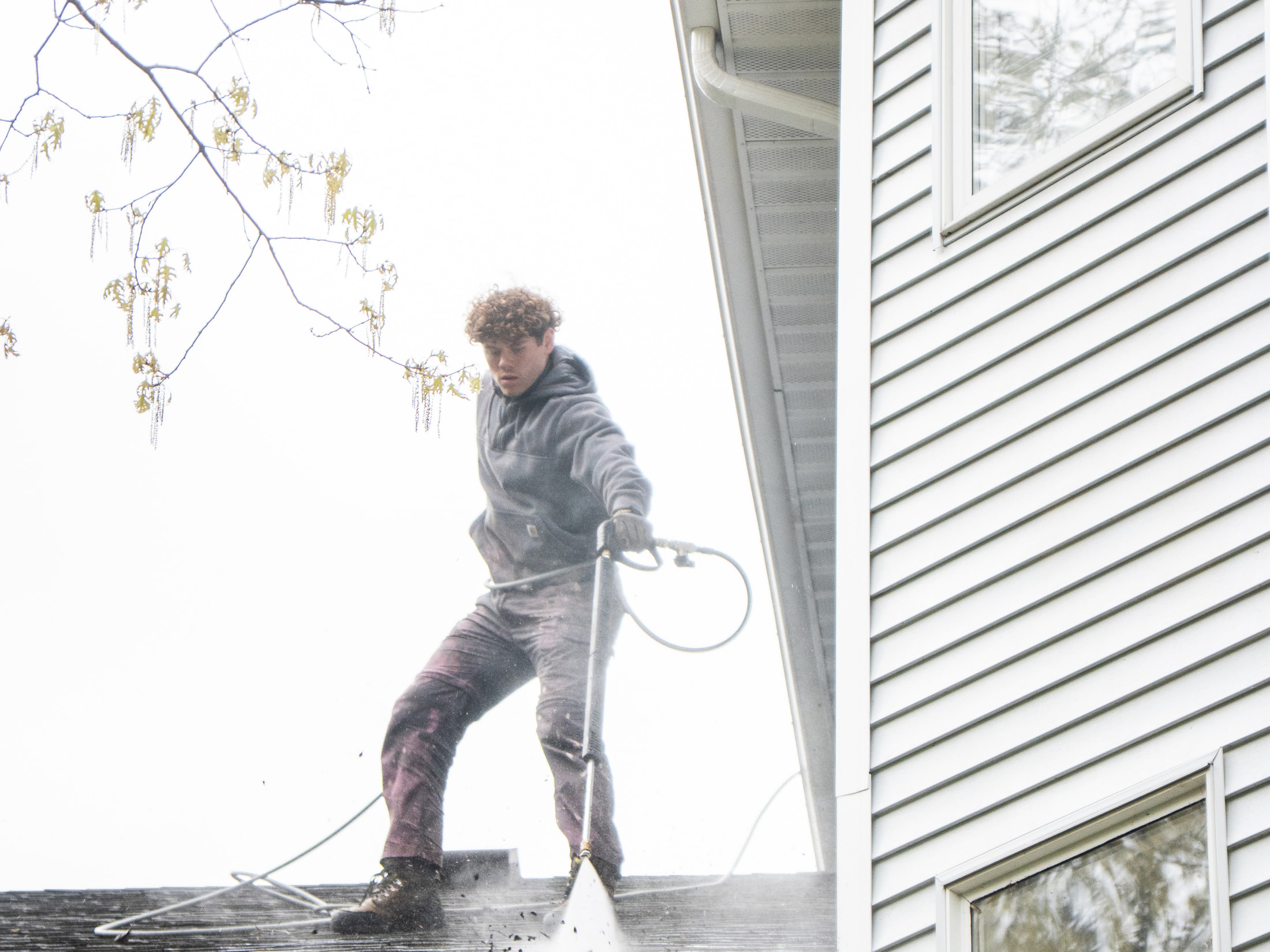 Technician clearing a home's gutters from the roof, debris flushing out over the roof edge