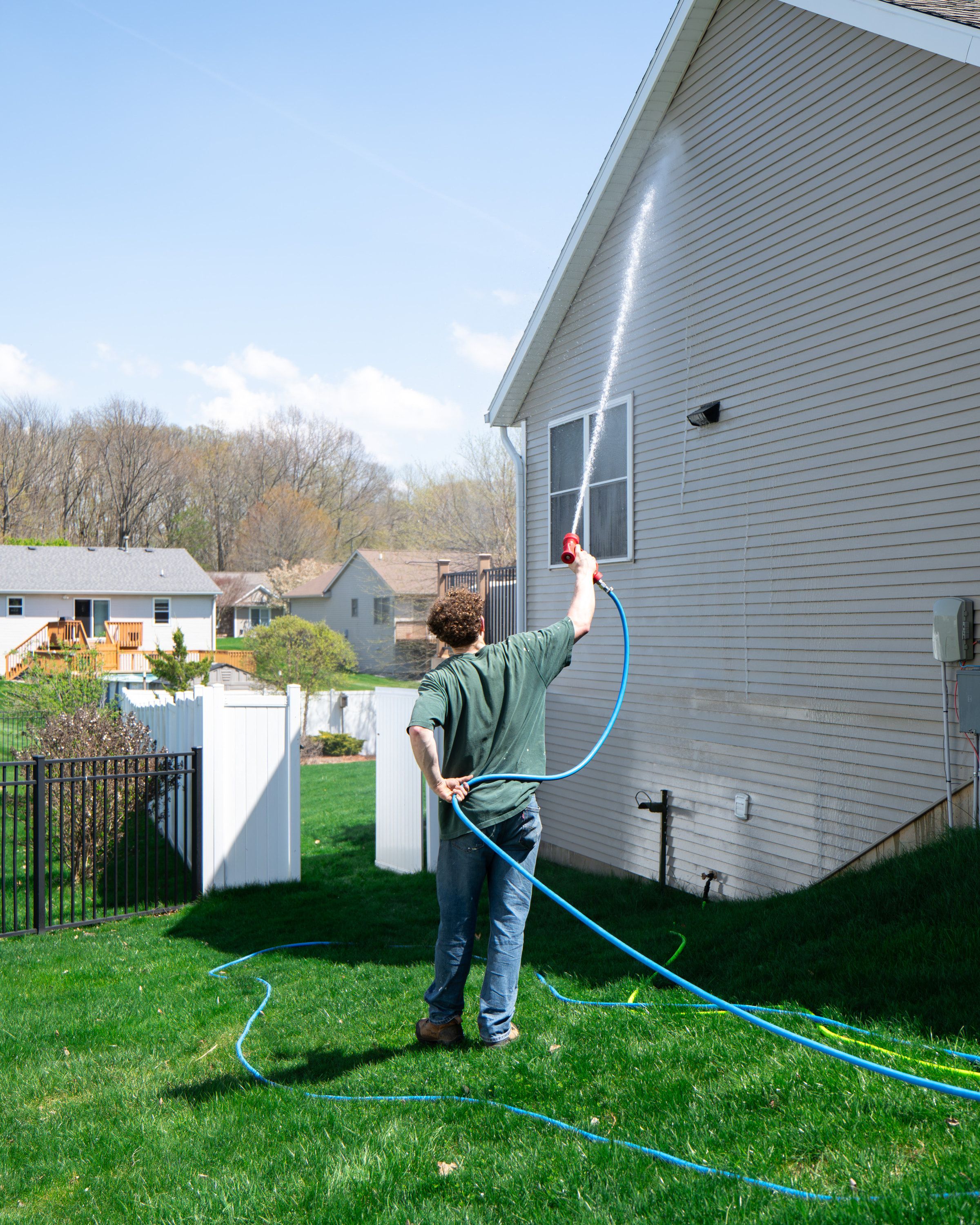 Elevation technician soft-washing the gable end of a two-story home from ground level with a low-pressure spray