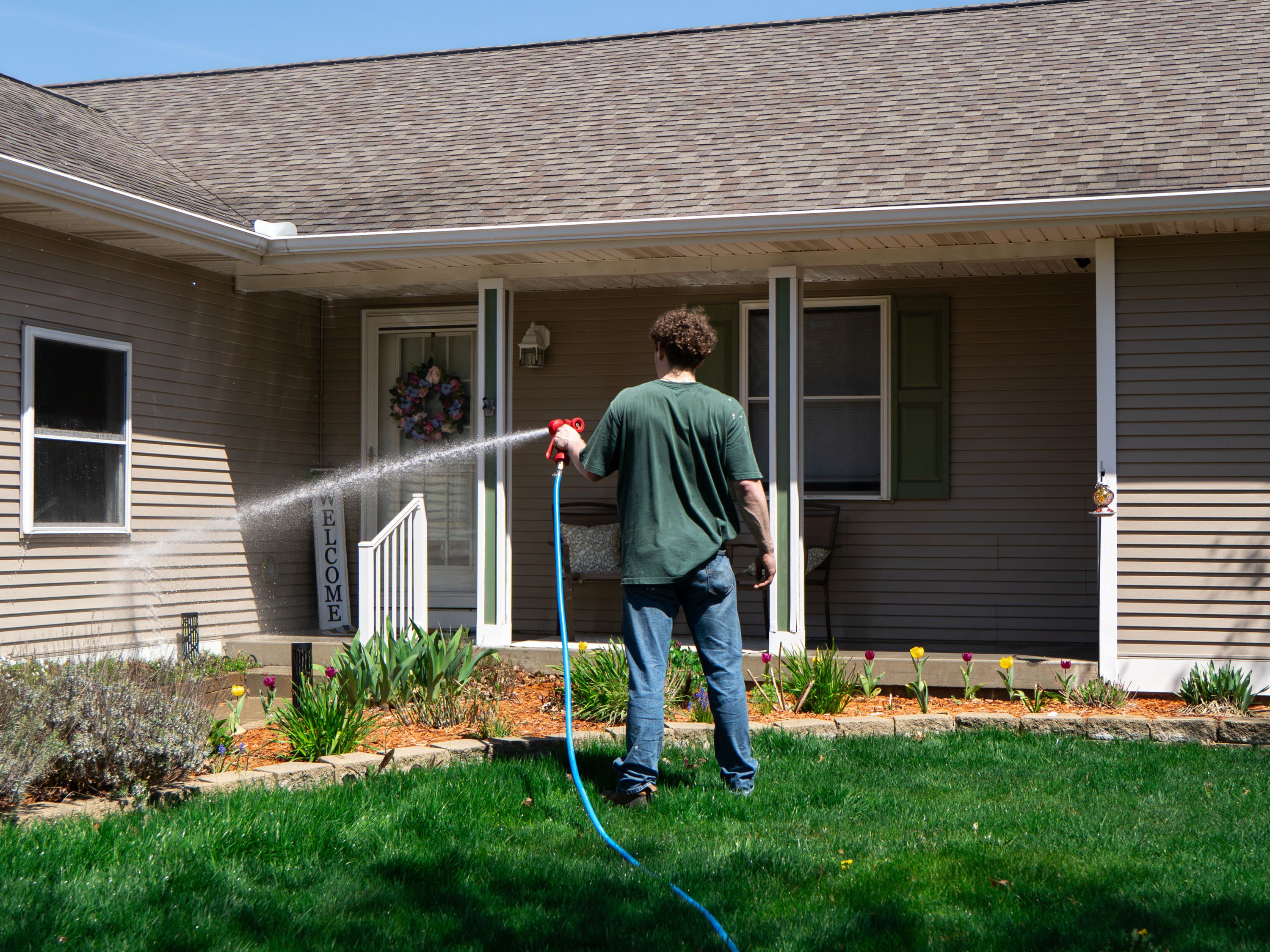 Elevation technician soft-washing the front of a home in the Jenison area from ground level