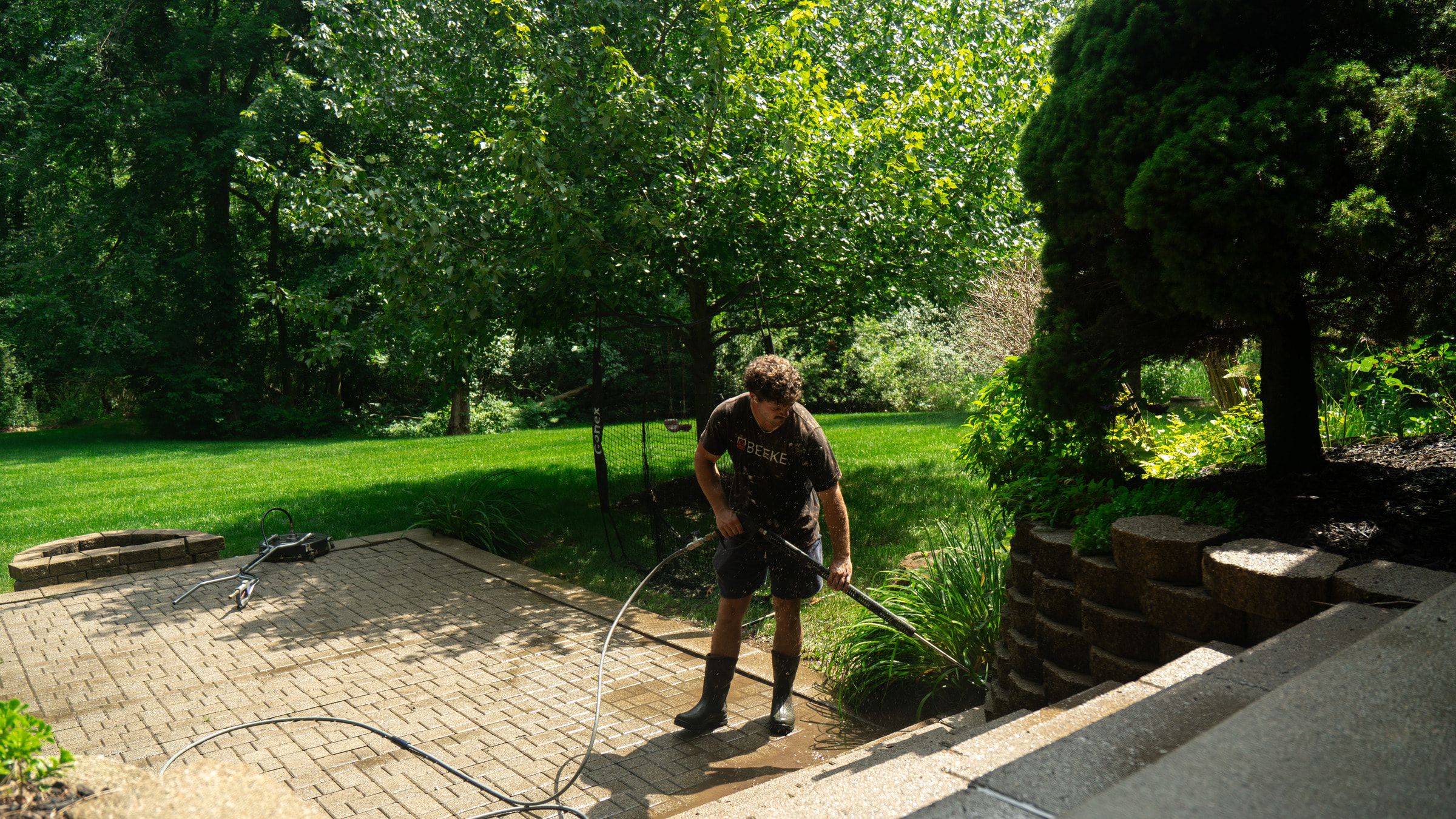 Elevation technician cleaning the edge of a paver patio beside a stone retaining wall