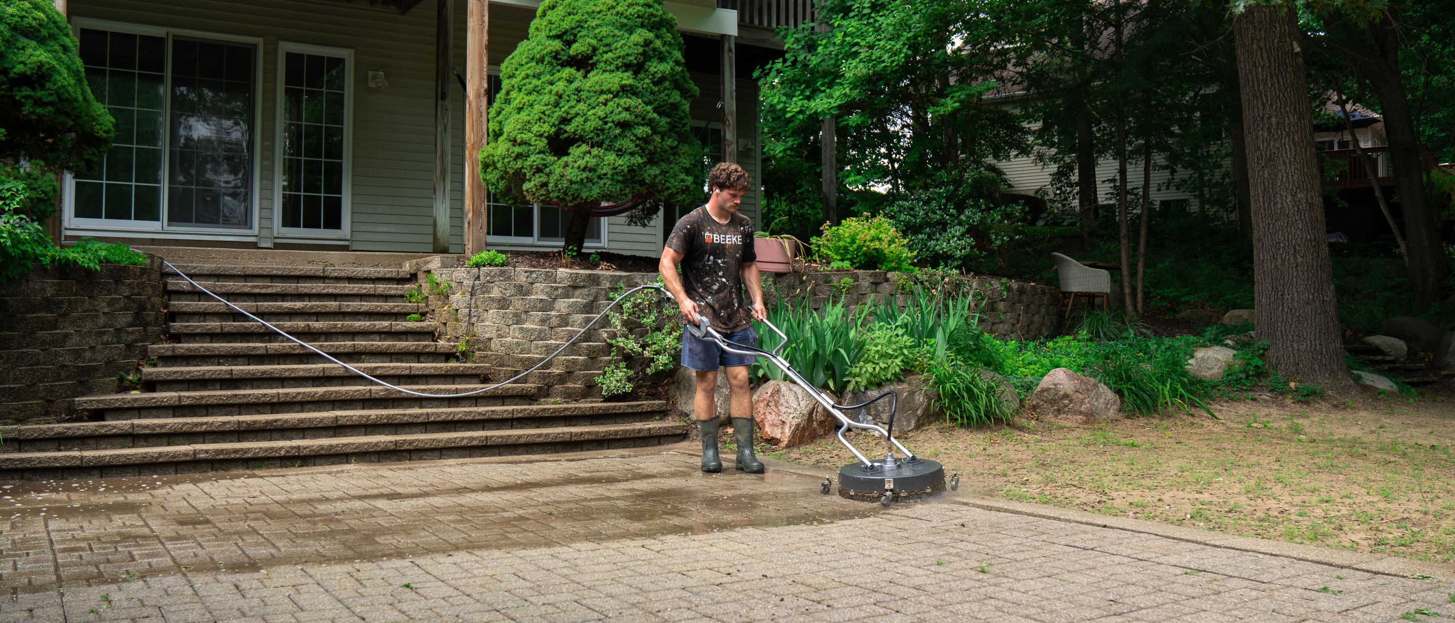 Rotary surface cleaner part-way across a brick paver patio, the cleaned pass visibly lighter than the pavers beside it
