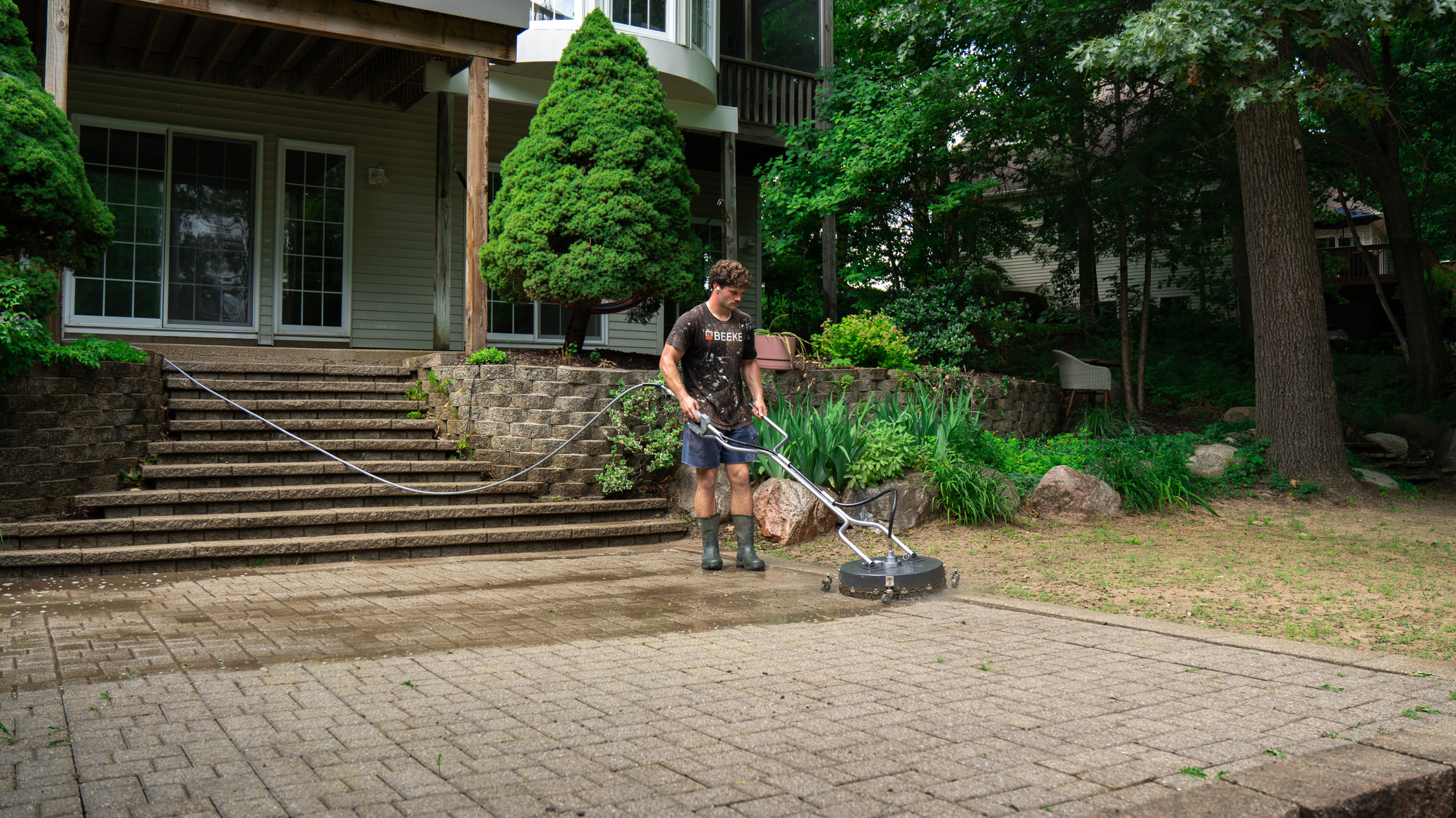 Rotary surface cleaner part-way across a paved surface — the cleaned pass visibly lighter than the stone beside it, the same process used for industrial & warehouse in the Grand Rapids metro