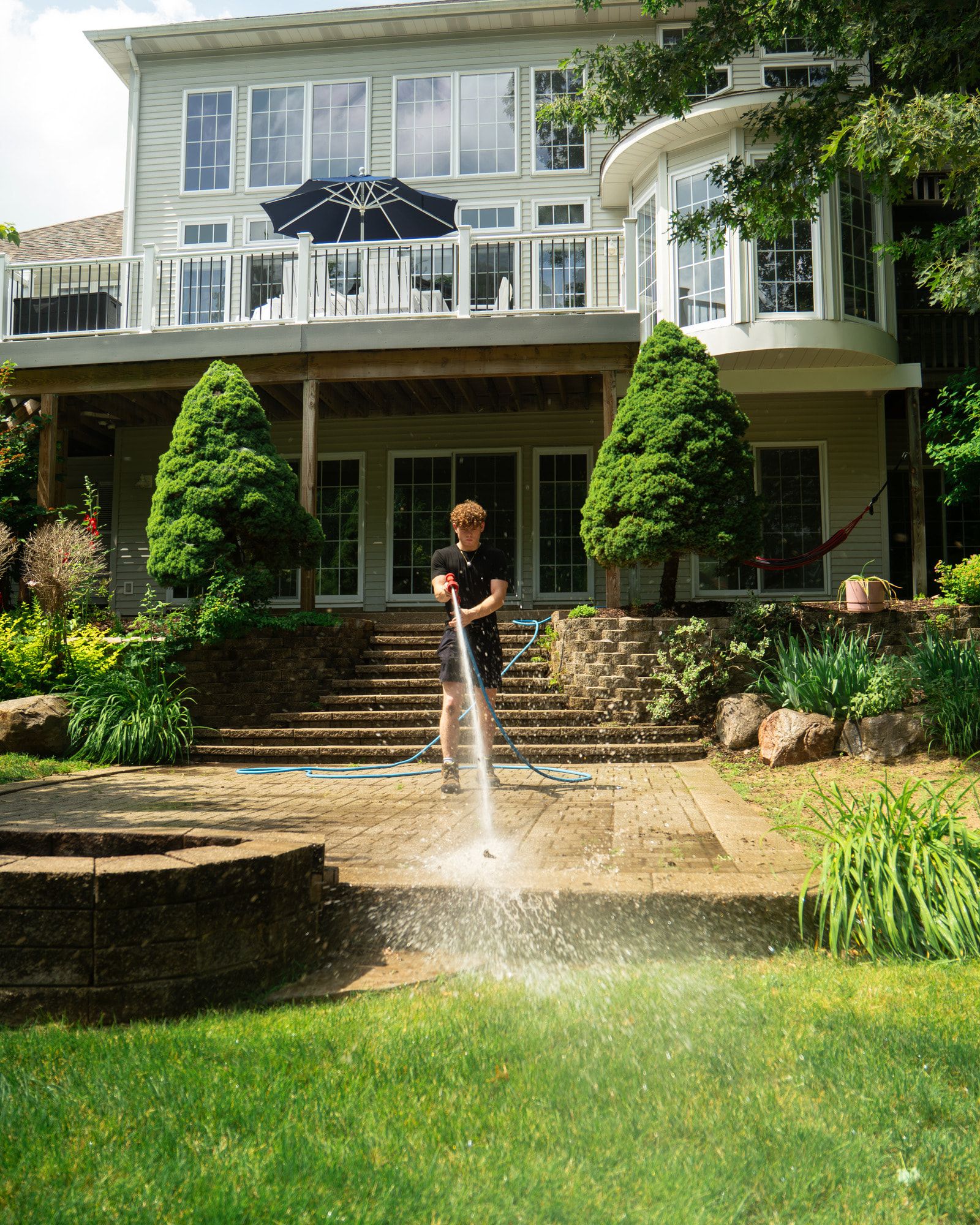 Elevation technician cleaning a brick paver patio with a low-angle wand, the cleaned pass visibly lighter