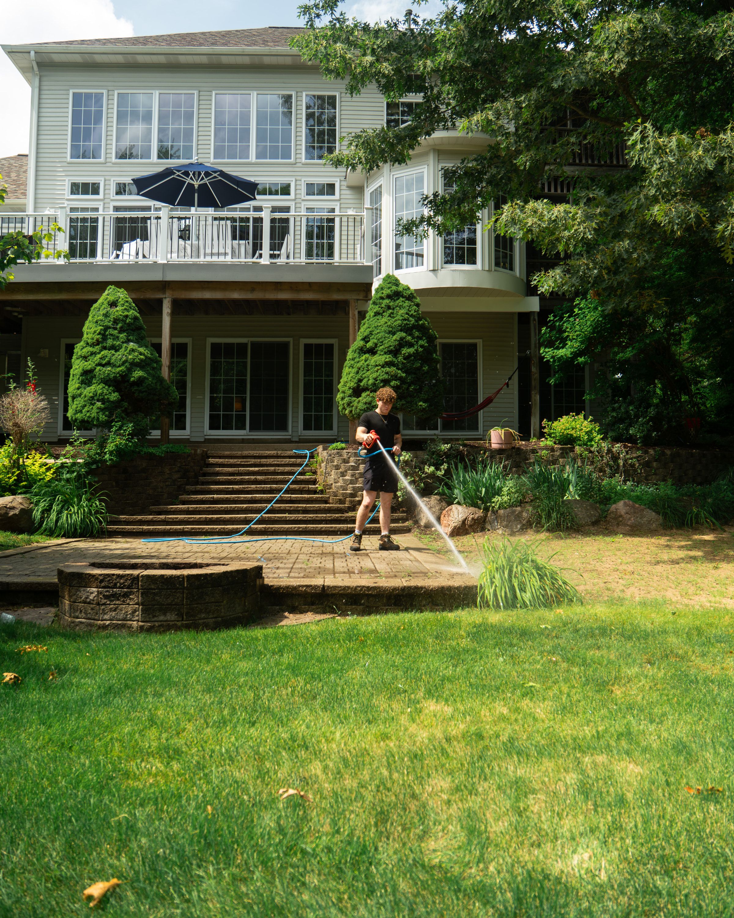 Wide view of a two-story home's backyard while an Elevation technician cleans the lower paver patio
